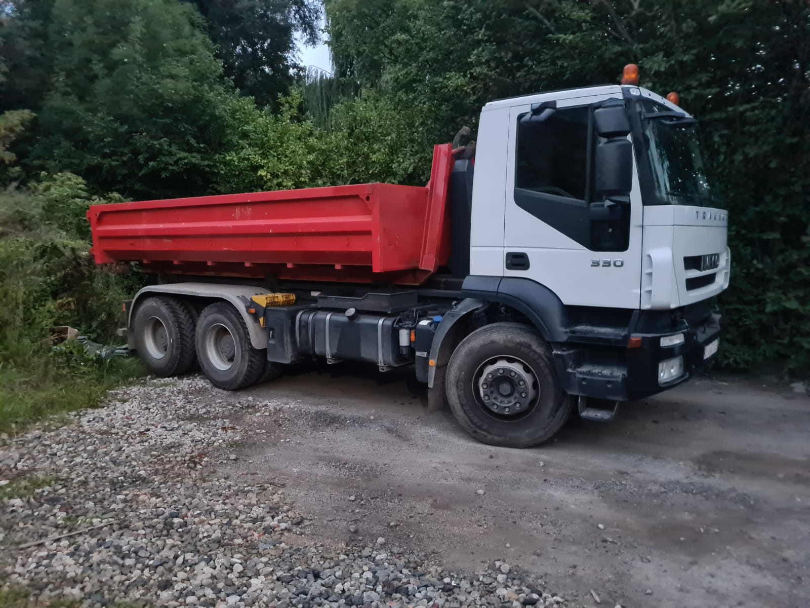 Un camion-benne blanc et rouge garé sur une route de gravier.